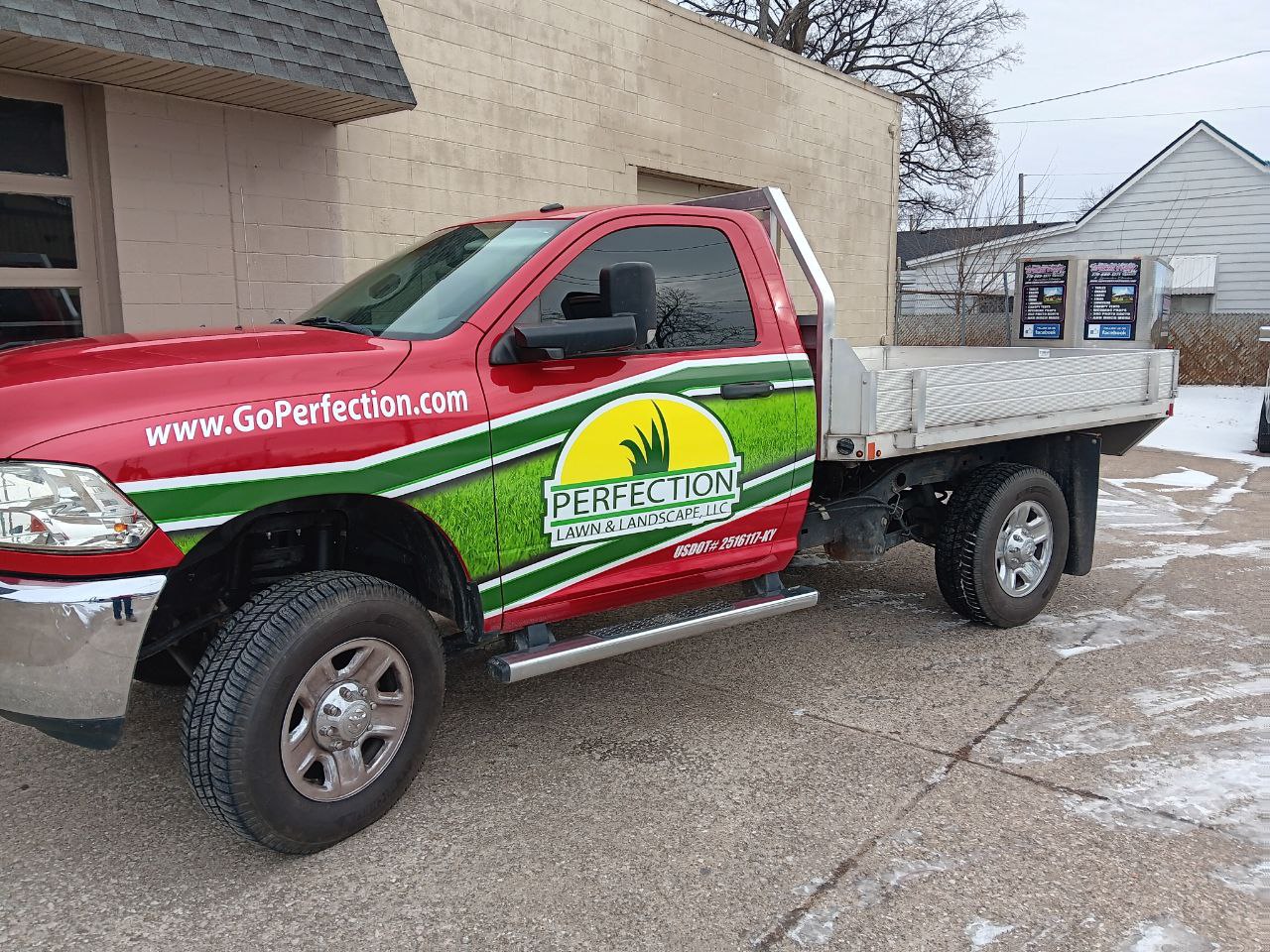 Perfection-About Us - 1 A red Perfection Lawn & Landscape truck with a flatbed parked on a snowy lot, featuring the company logo and website URL.
