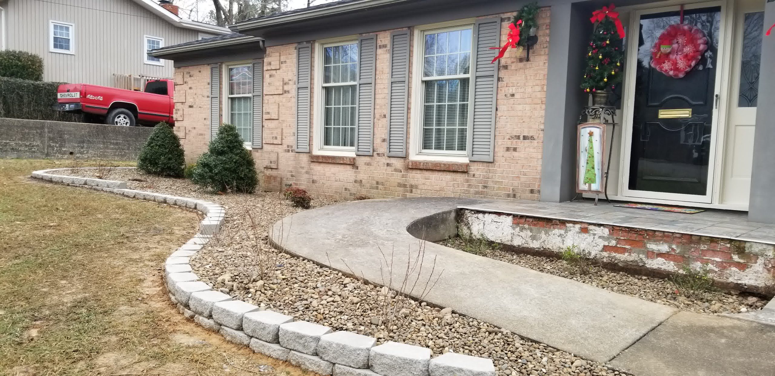 go perfection concrete work manor tx driveways sidewalks patios scaled - Perfection Lawn & Landscape LLC Curved stone garden edging borders gravel beds and shrubs in front of a brick house, adding curb appeal and landscape definition.