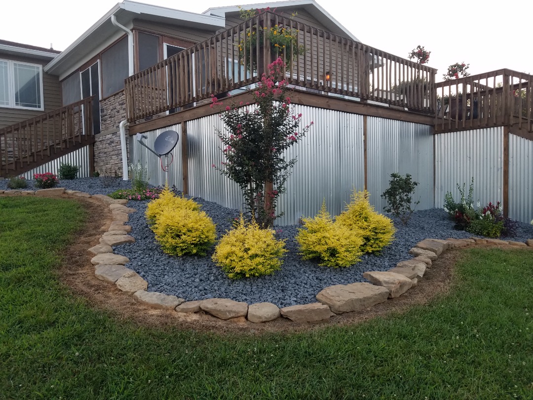 perfection lawn landscape greenville fall cleanups - Perfection Lawn & Landscape LLC Landscaped backyard with neatly trimmed yellow shrubs, black mulch, and stone border against a metal-sided raised deck.
